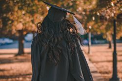 University graduate walking away under autumnal trees close up